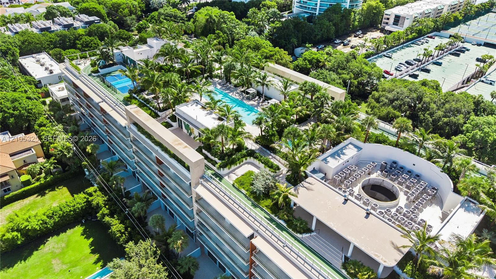 Modern multi-story building featuring multiple balconies, a structured rooftop area, and a lush green landscape