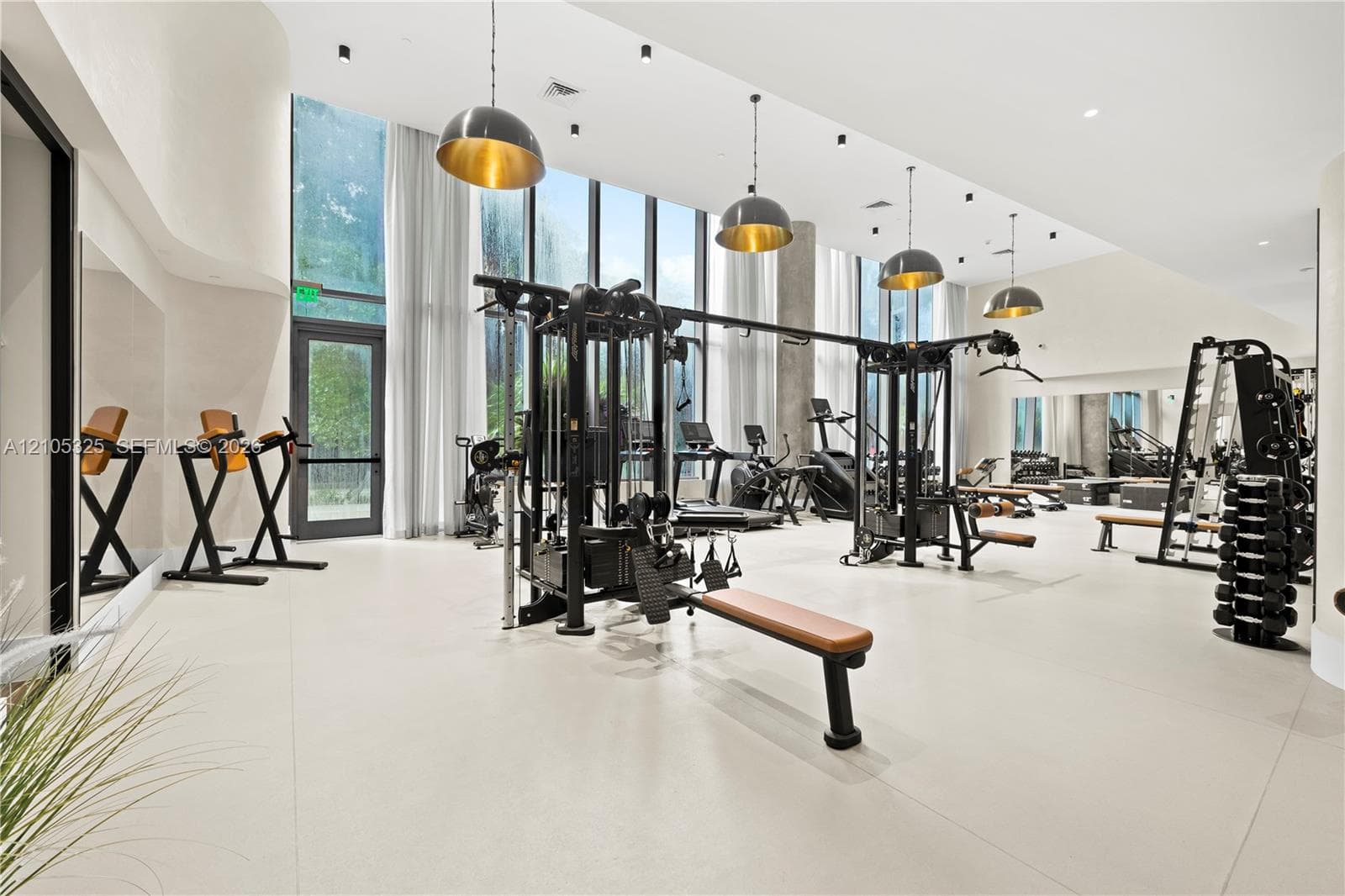 Expansive fitness center featuring high ceilings, floor-to-ceiling windows, recessed lighting, and multiple pendant light fixtures