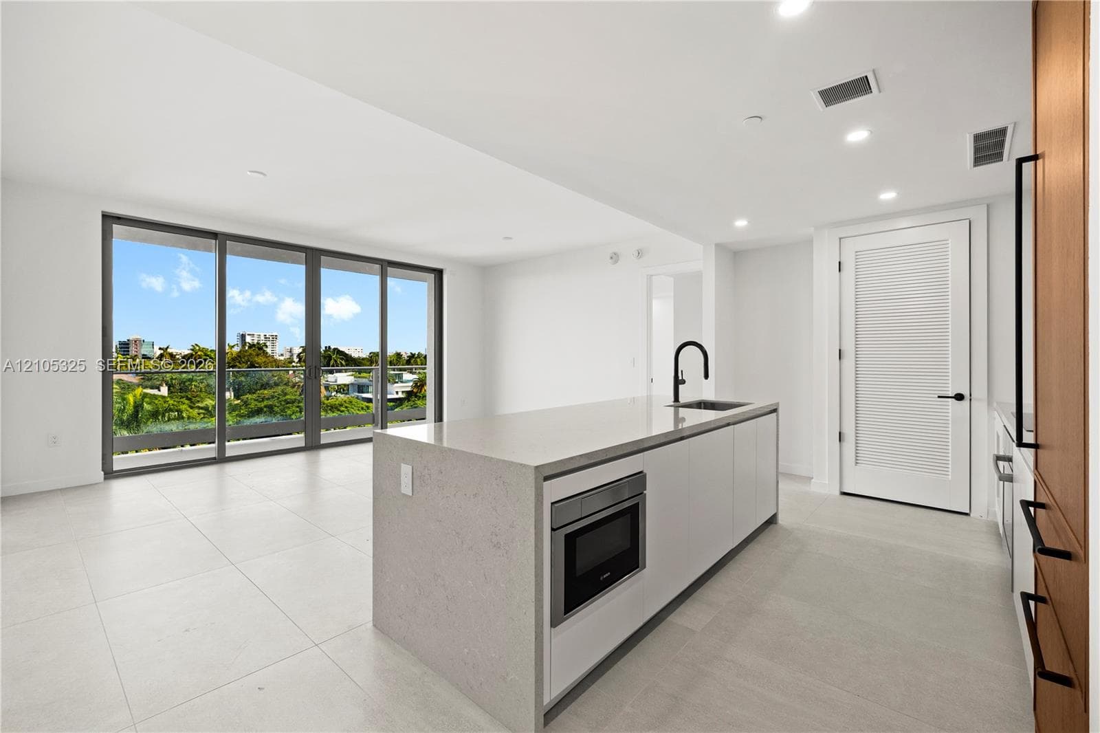 Open concept living space featuring a large sliding glass door, an expansive kitchen island with an integrated microwave, a built-in sink with a black faucet, and light tile flooring