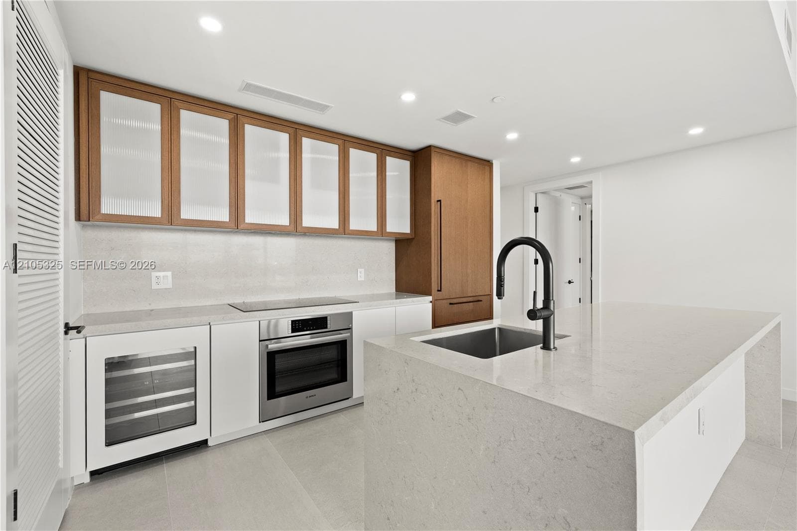 Modern kitchen featuring white quartz countertops, stainless steel dual wall ovens with integrated microwave, wine refrigerator, and a professional-style pull-down faucet