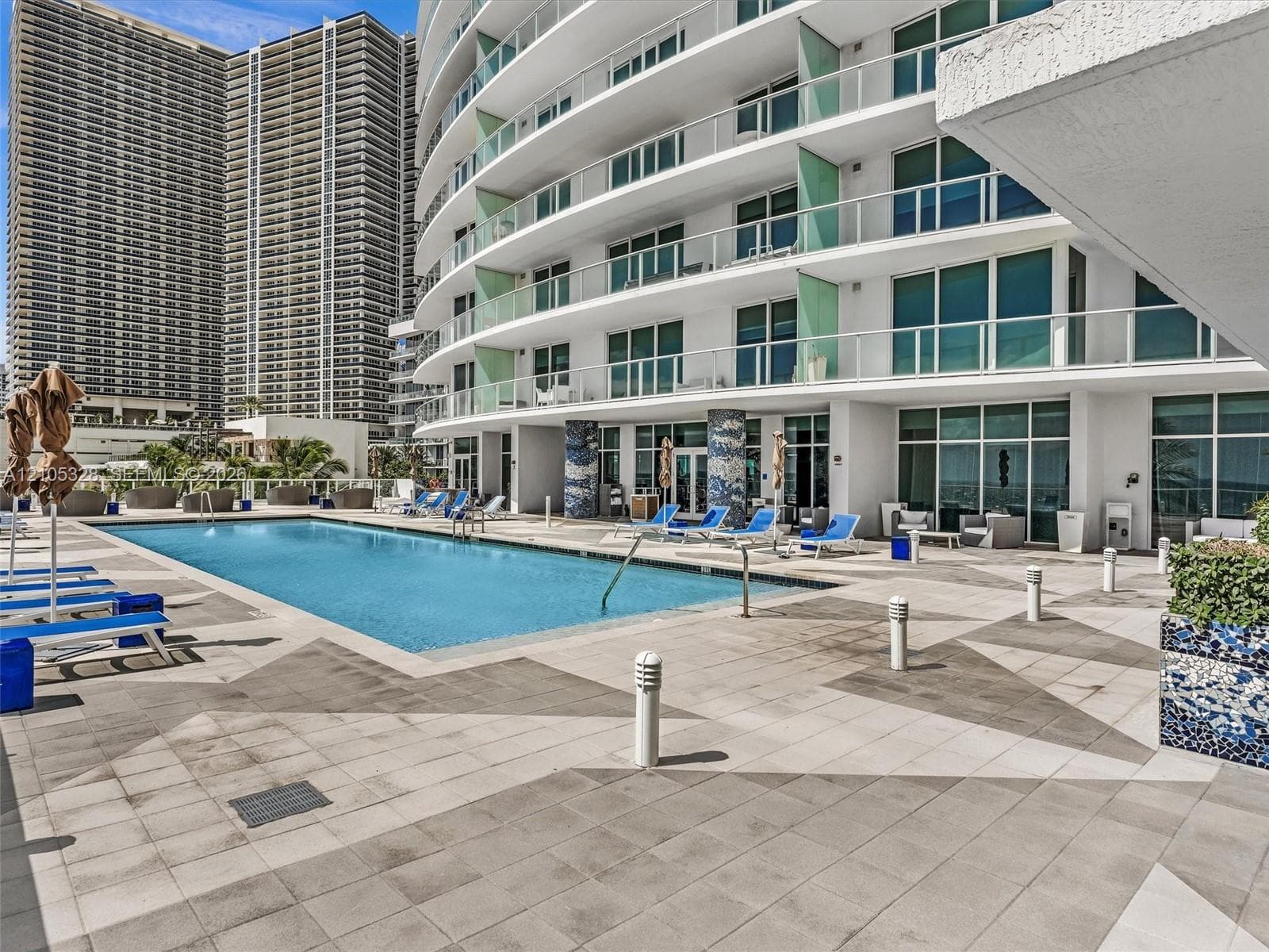 Experience oceanfront resort-style living at Apogee Beach, featuring an inviting swimming pool, expansive pool deck, sleek glass railings, and direct access to the beach and Atlantic Ocean.