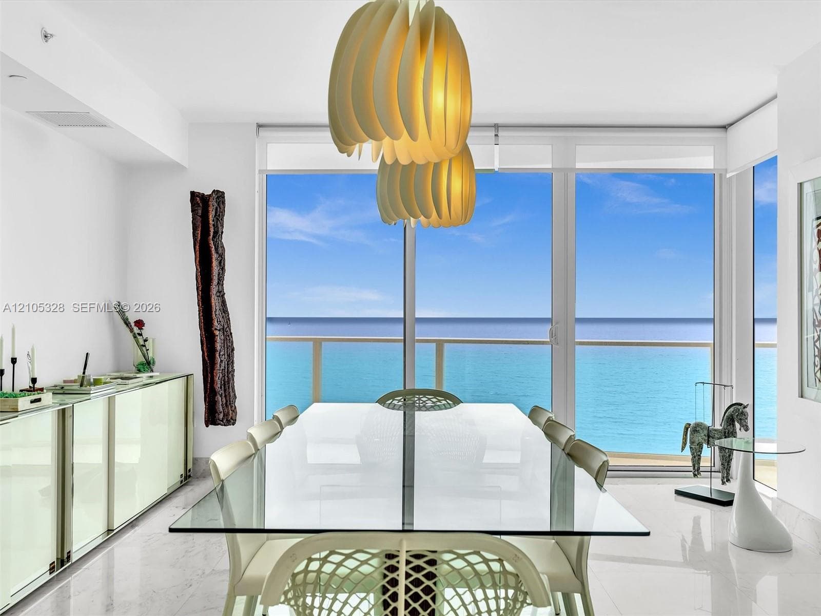 Elegant dining area featuring floor-to-ceiling glass doors and windows, large-format tile flooring, contemporary pendant lighting, and a glass-top dining table.