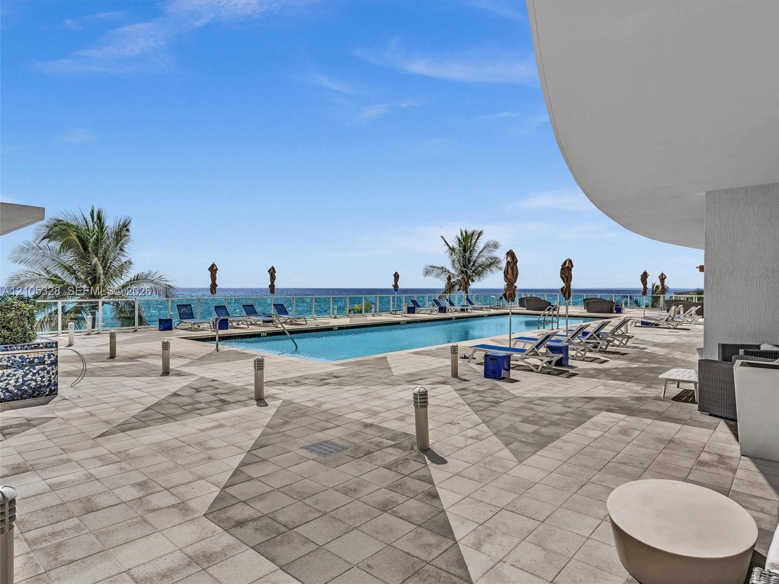 Experience oceanfront resort-style living at Apogee Beach, featuring an inviting swimming pool, expansive pool deck, sleek glass railings, and direct access to the beach and Atlantic Ocean.