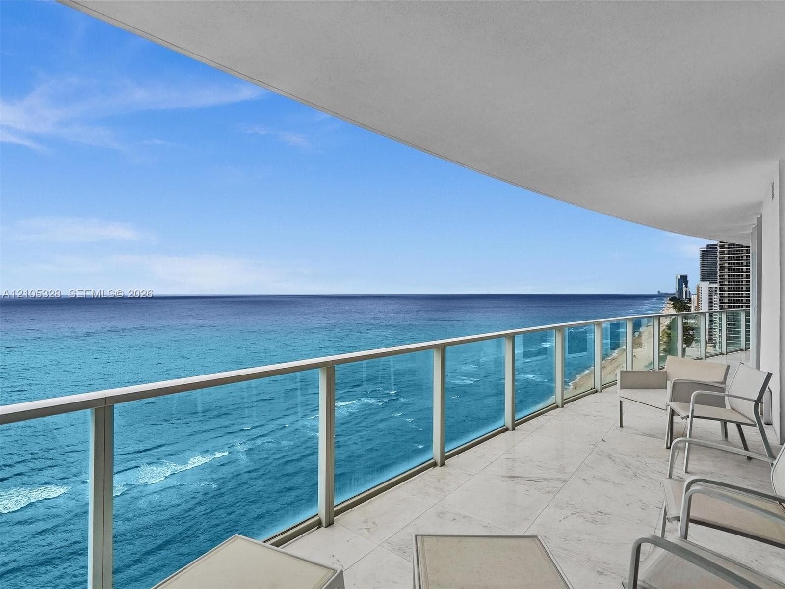 Expansive private balcony featuring glass railings, stone tile flooring, and unobstructed ocean views.
