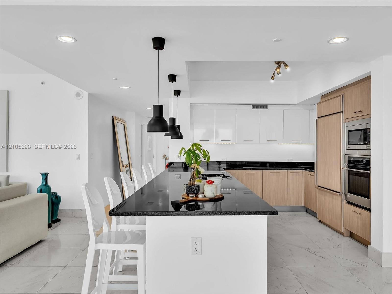 Modern gourmet kitchen featuring an oversized center island with seating, sleek dark stone countertops, stainless steel appliances, and wood-finish cabinetry.