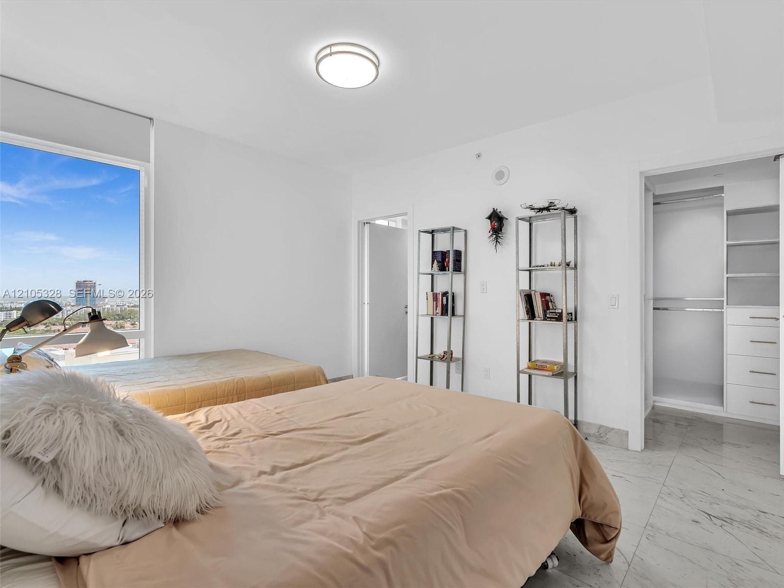 Bright and elegantly appointed interior featuring an expansive window that fills the space with natural light, a custom built-in closet organization system, polished stone flooring, crisp white walls, and recessed ceiling lighting.