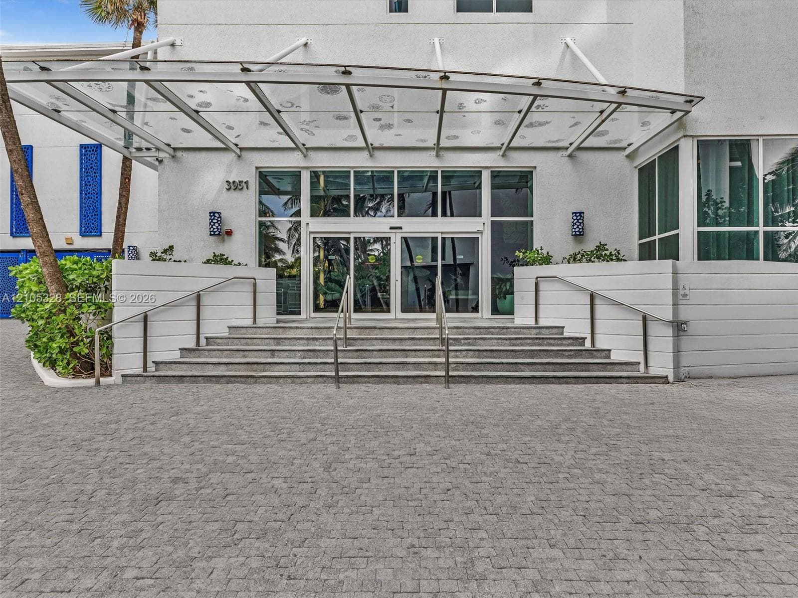 Elegant building entrance featuring a contemporary glass canopy, beautifully paved entryway, and sleek stainless steel railings, creating a sophisticated arrival experience.