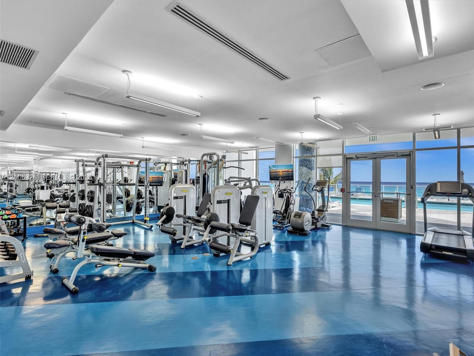 Expansive fitness center featuring a blue and dark blue patterned floor, floor-to-ceiling windows, and abundant natural light