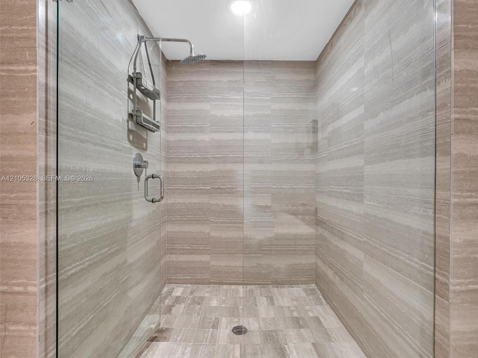 Luxurious spa-inspired shower featuring a frameless glass enclosure, ceiling-mounted rainfall showerhead, handheld shower, and elegant horizontally patterned wall tiles.