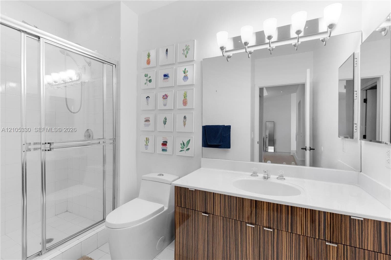 Shower with glass enclosure, single vanity with wood-finish cabinetry, white countertop, and integrated sink