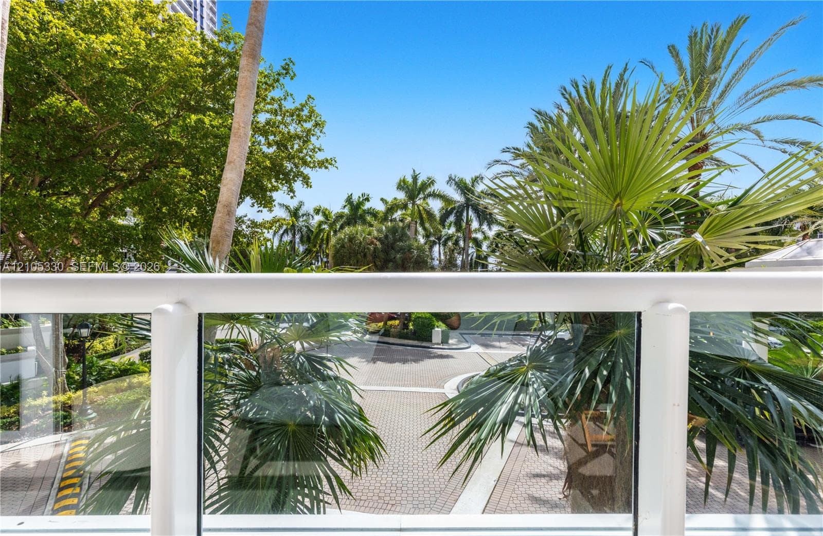 Balcony with glass railing overlooking mature palm trees and lush landscaping