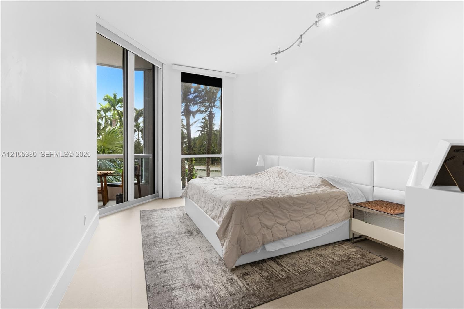 Expansive floor-to-ceiling windows, track lighting, light-toned flooring, and a sliding glass door leading to a balcony