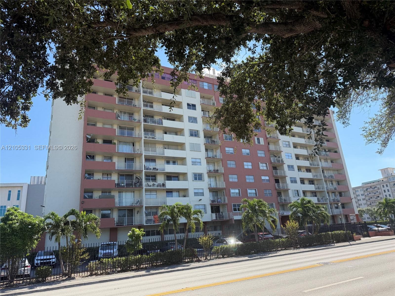 Multi-story high-rise exterior featuring individual recessed balconies, concrete construction, and perimeter fencing
