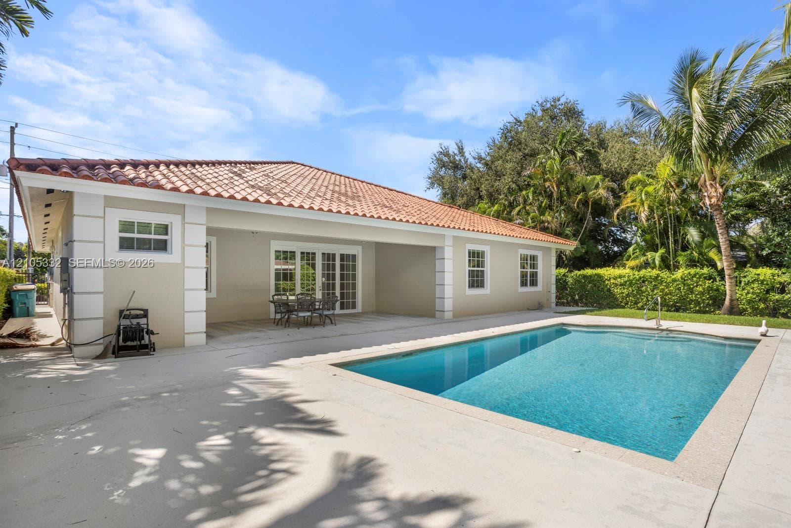Swimming pool with a surrounding concrete patio, terracotta tile roof, and French doors opening to an outdoor patio space