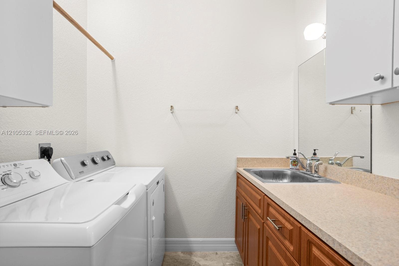 Laundry area with light-toned countertop, wood-finish cabinetry, and a stainless steel utility sink