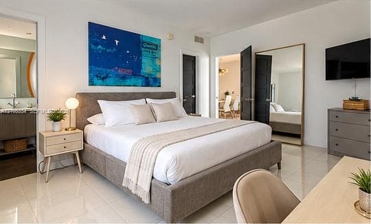 White tile flooring throughout, large full-length mirror, dark paneled doors, and an adjoining space with a vanity