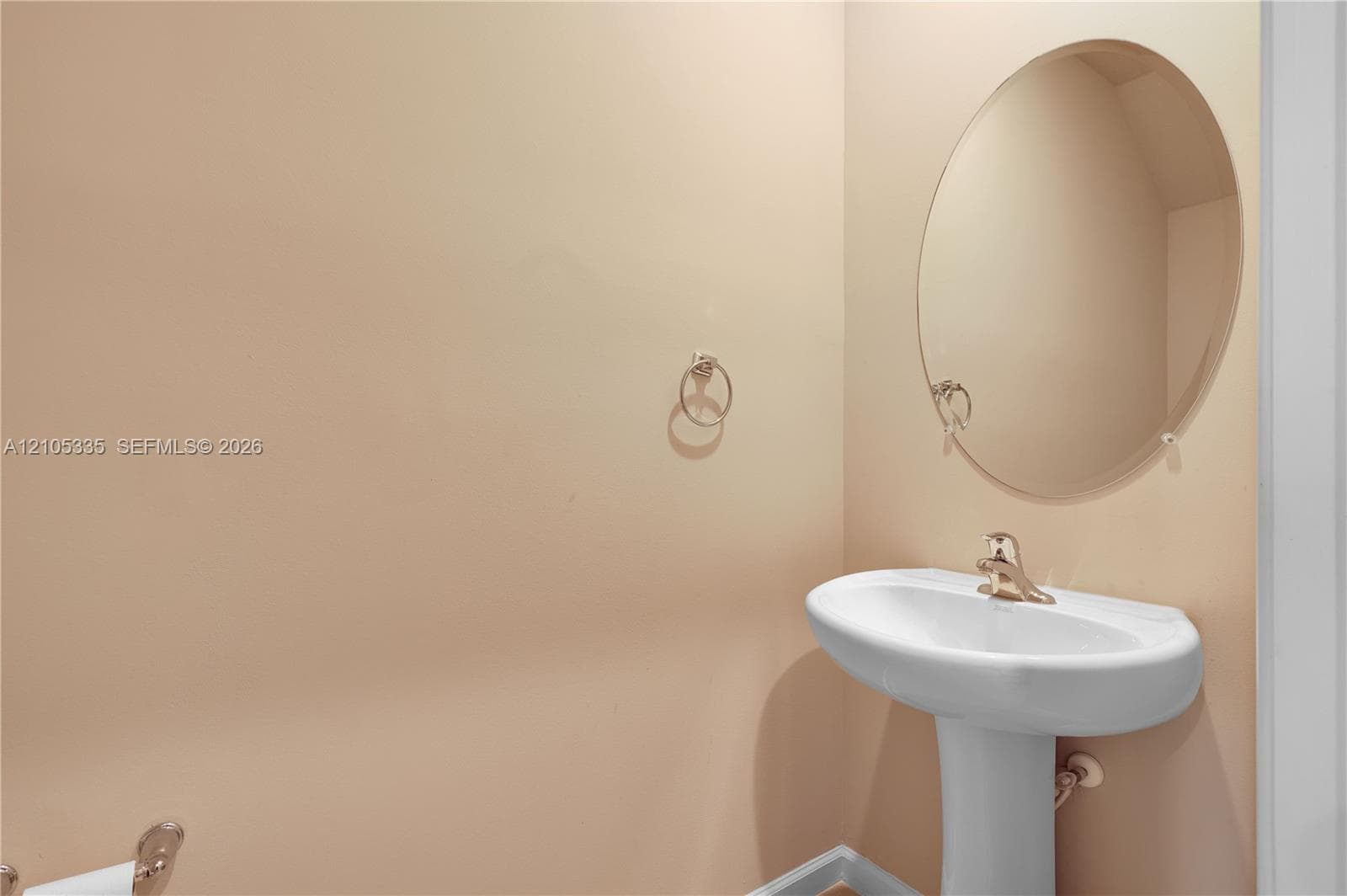 Pedestal sink with a polished brass faucet, oval wall-mounted mirror, and neutral wall color