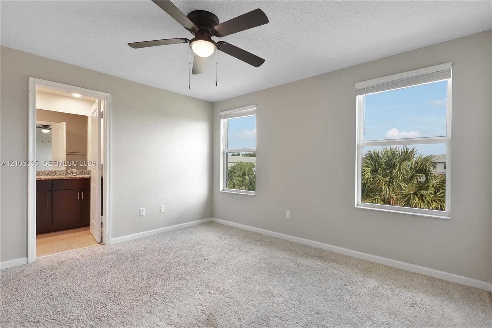 Carpeted room with a ceiling fan, two windows, and an en-suite bathroom featuring a vanity with a stone countertop and dark wood-finish cabinetry