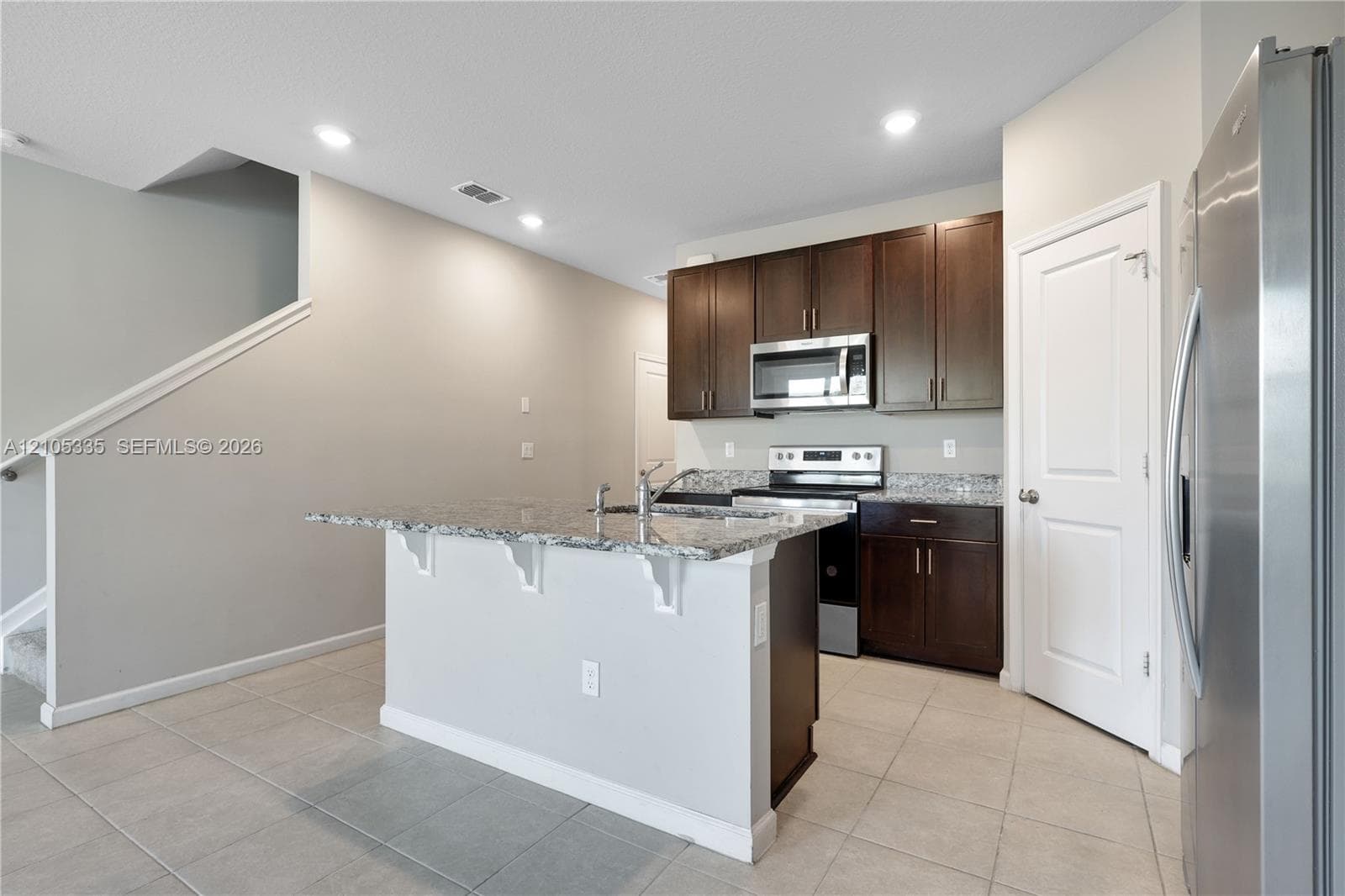 Kitchen featuring dark wood-finish cabinetry, stainless steel appliances, granite countertops, and a central island with sink