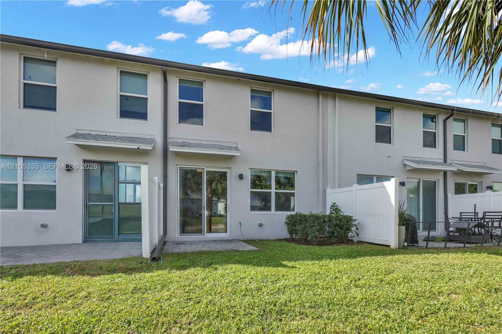 Expansive green space with stucco exterior, sliding glass doors, upper-level windows, and privacy fencing