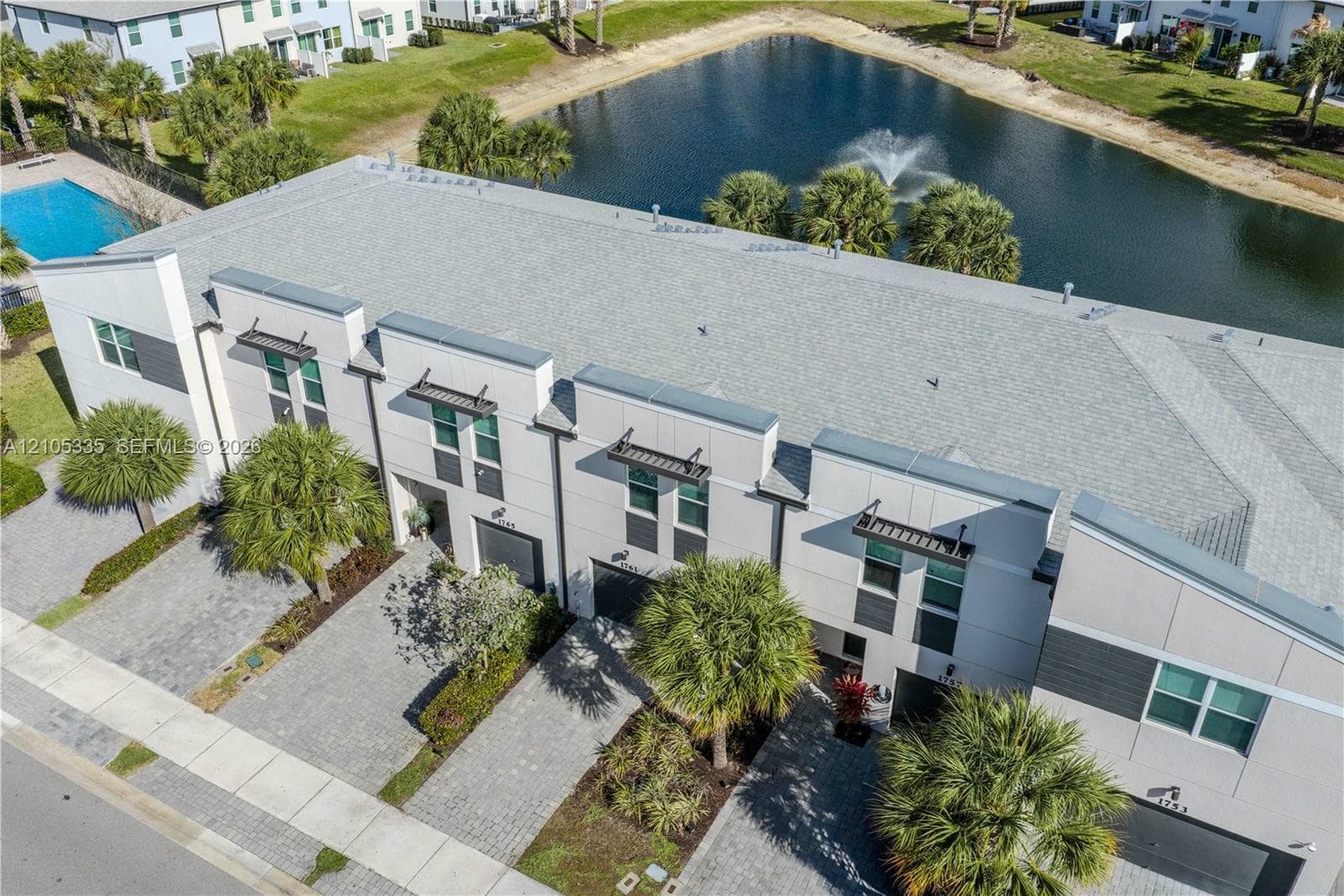 Modern townhome exterior with light gray siding, paver driveways, and mature landscaping