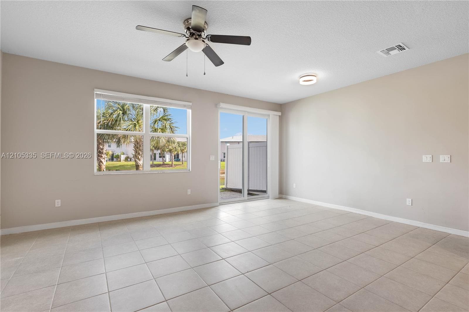 Recessed ceiling lighting, a ceiling fan, and large tile flooring define this bright room with a sliding glass door and an expansive window