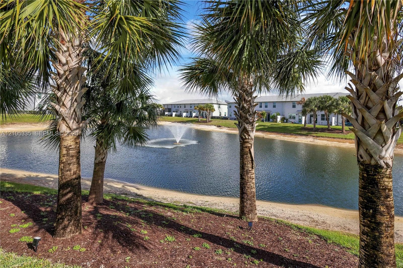 Waterfront location featuring a fountain, sandy bank, and lush landscaping with mature palm trees