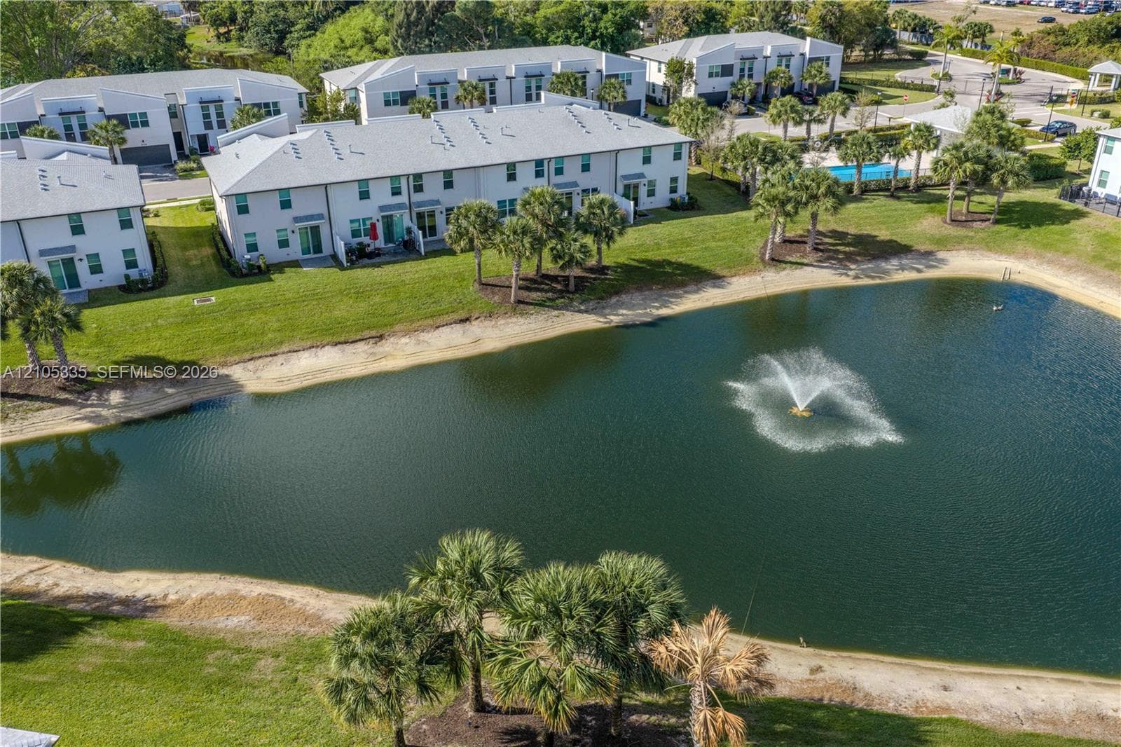 Waterfront property with a fountain, featuring a sandy shoreline and mature palm trees
