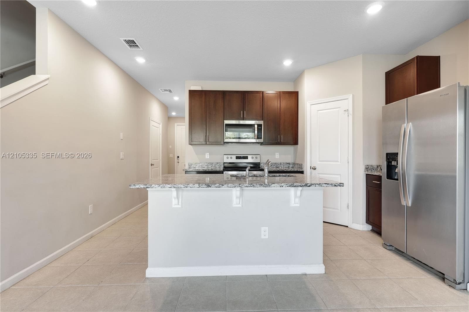 Kitchen featuring a central island with a stone countertop, dark wood-finish cabinetry, stainless steel appliances, and tiled flooring