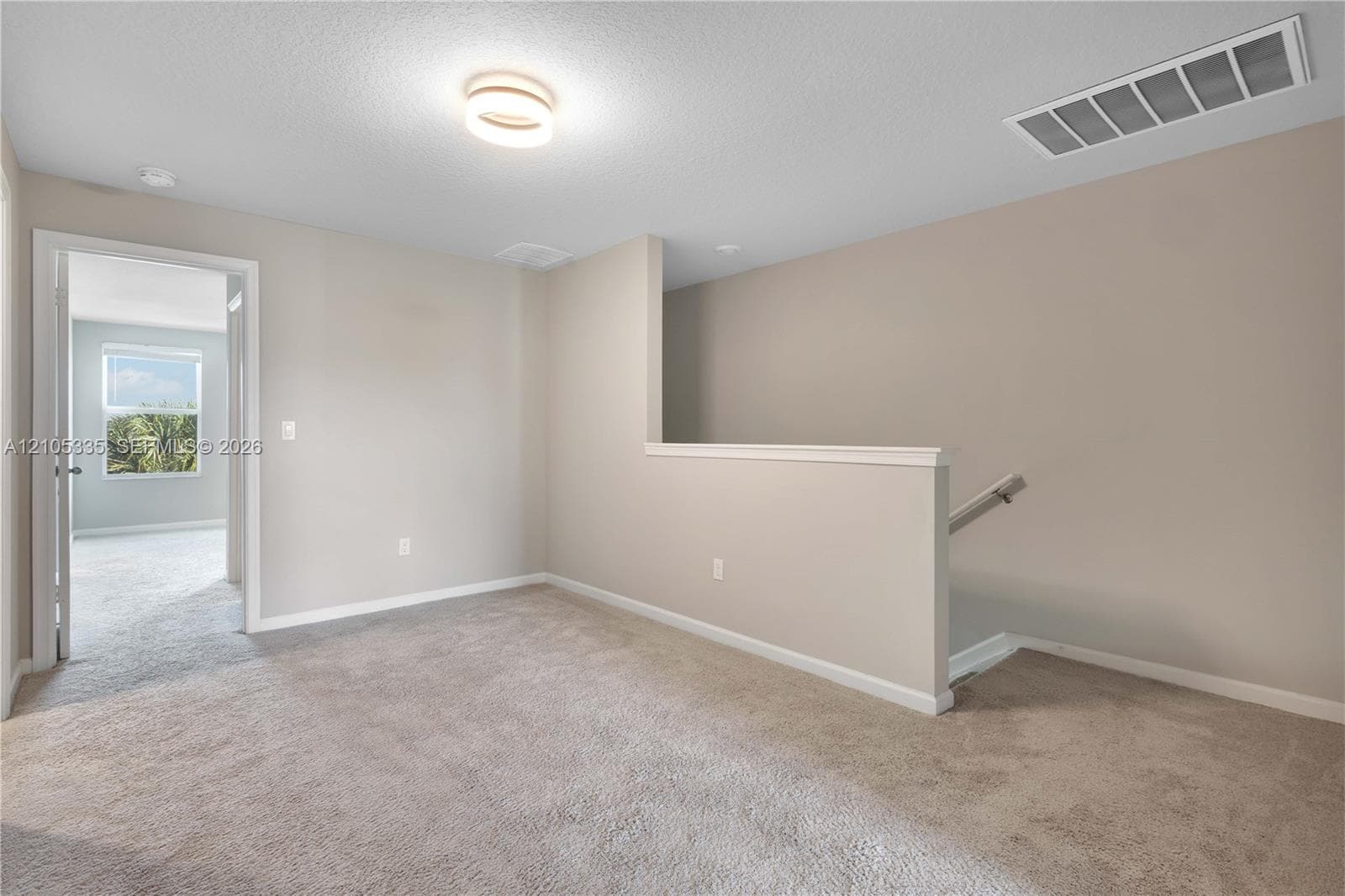 Carpeted area featuring light-toned walls, a modern flush-mount ceiling light, and a half-wall partition with a white cap