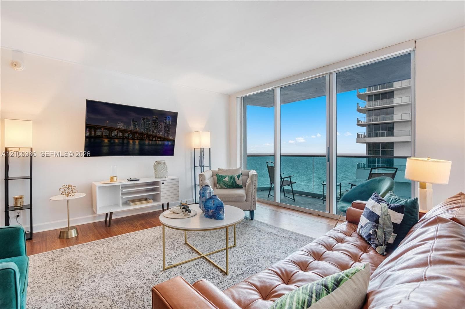 Living area featuring expansive floor-to-ceiling glass sliding doors, private balcony, and polished wood-finish flooring
