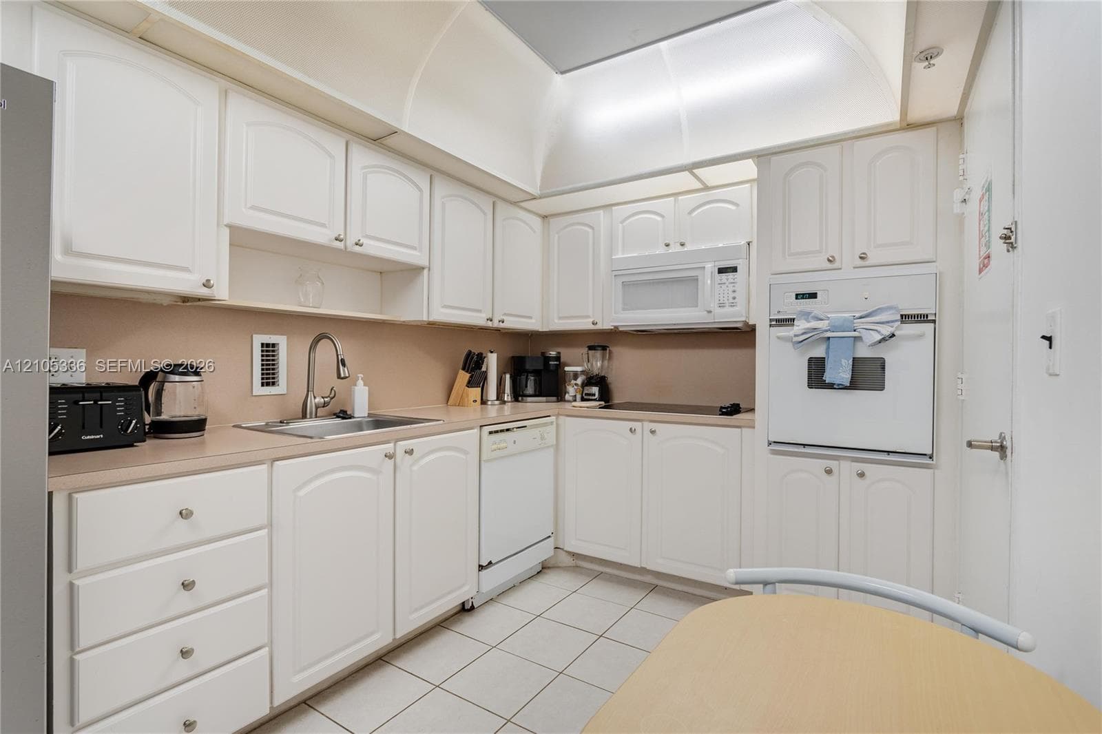 Kitchen featuring white cabinetry, integrated white appliances, arched ceiling detail, and light-toned countertops