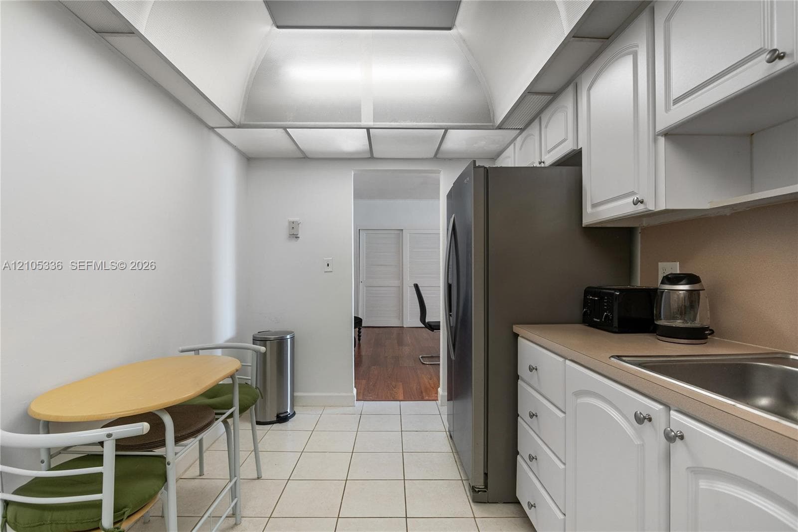 Kitchen featuring white shaker-style cabinetry, solid-surface countertops, a stainless steel refrigerator, ceramic tile flooring, and recessed tray ceiling lighting