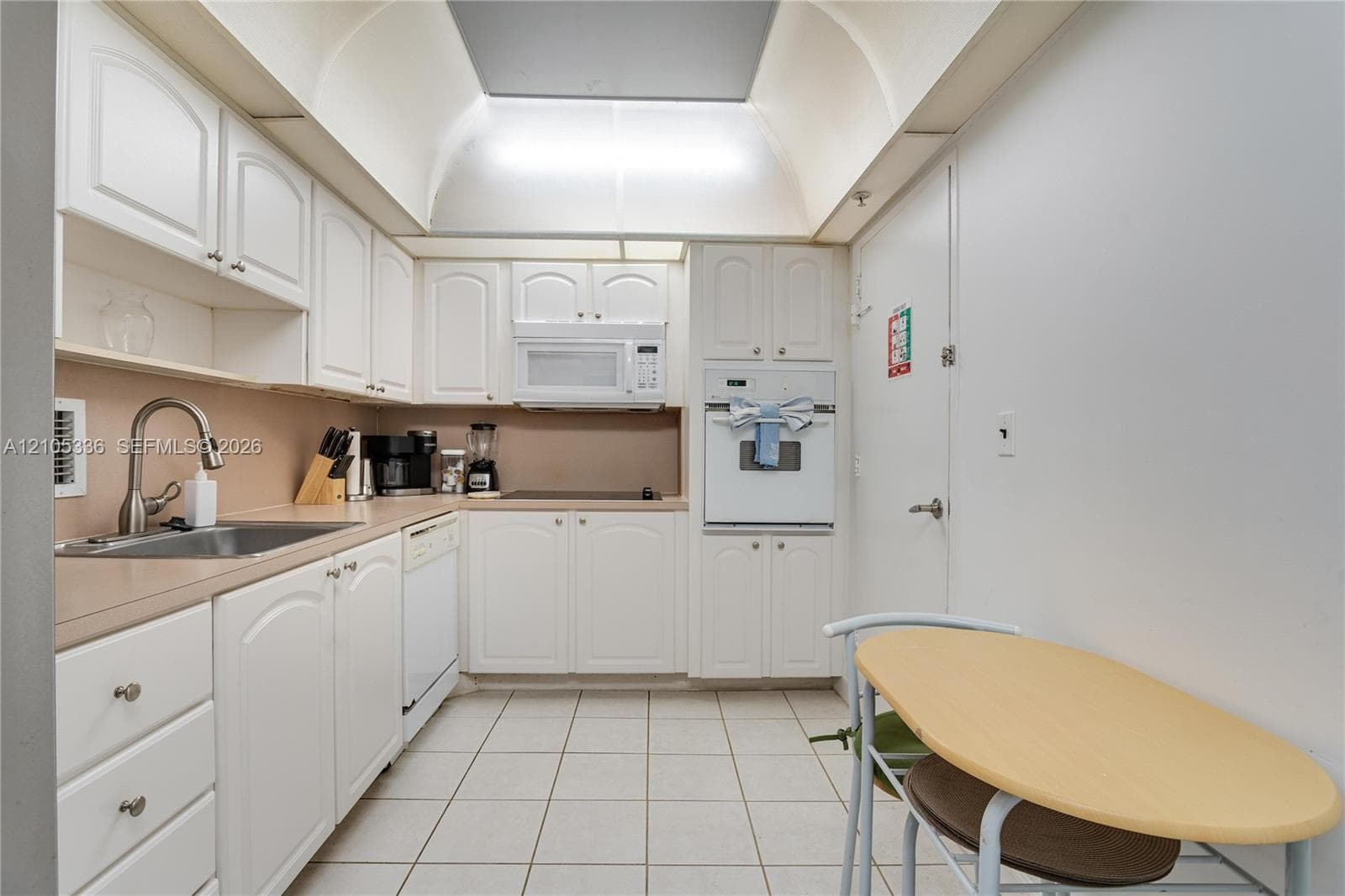 Kitchen featuring white cabinetry, vaulted ceiling with recessed lighting, tile flooring, integrated wall oven, and stainless steel sink with high-arc faucet