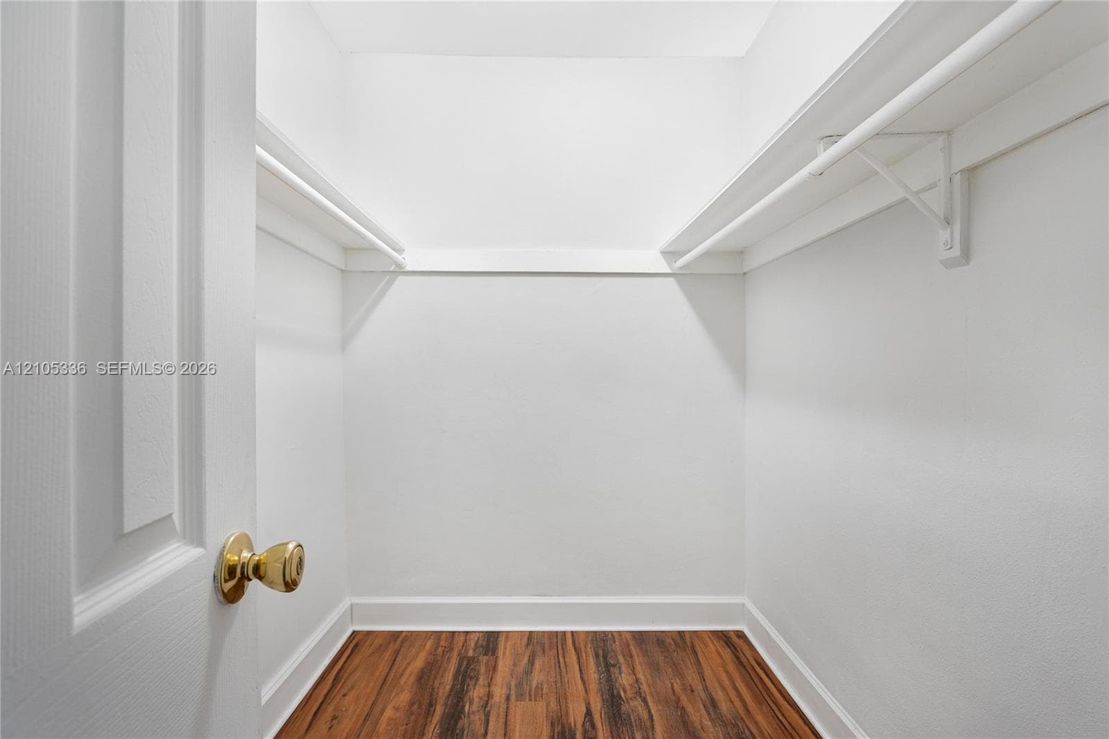 Storage closet featuring wood-finish flooring, white walls, and built-in shelving with integrated rods