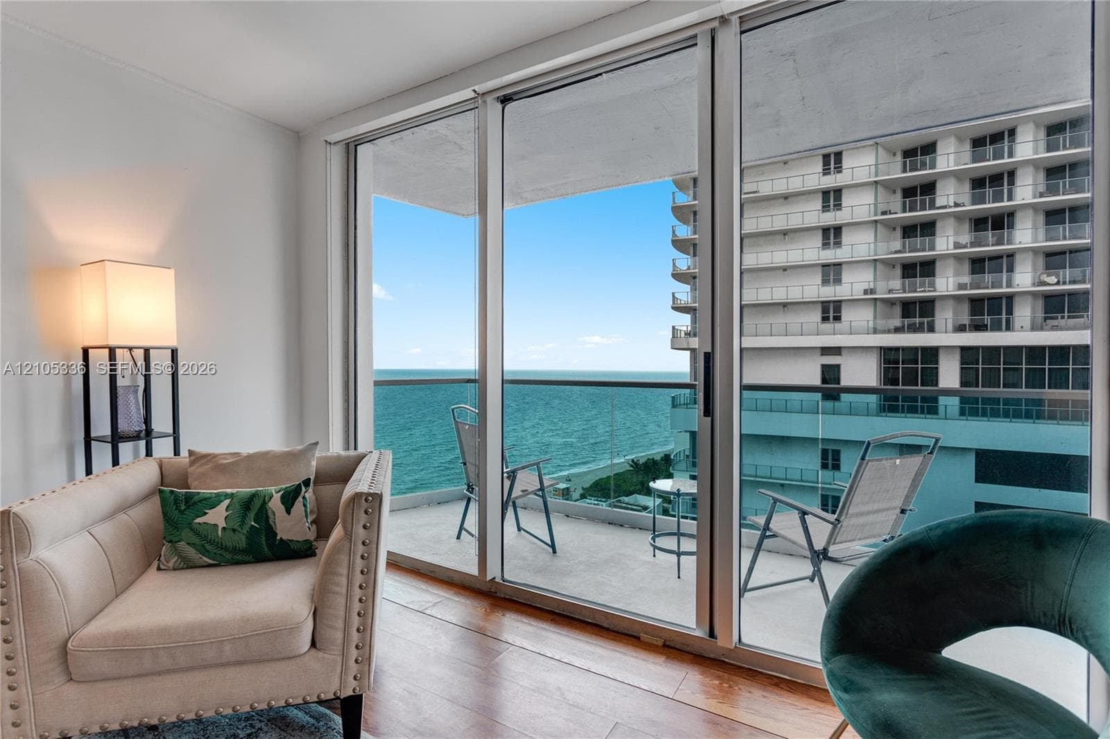 Floor-to-ceiling glass sliding doors opening to an expansive balcony with a glass railing, wood-finish flooring, and ocean exposure