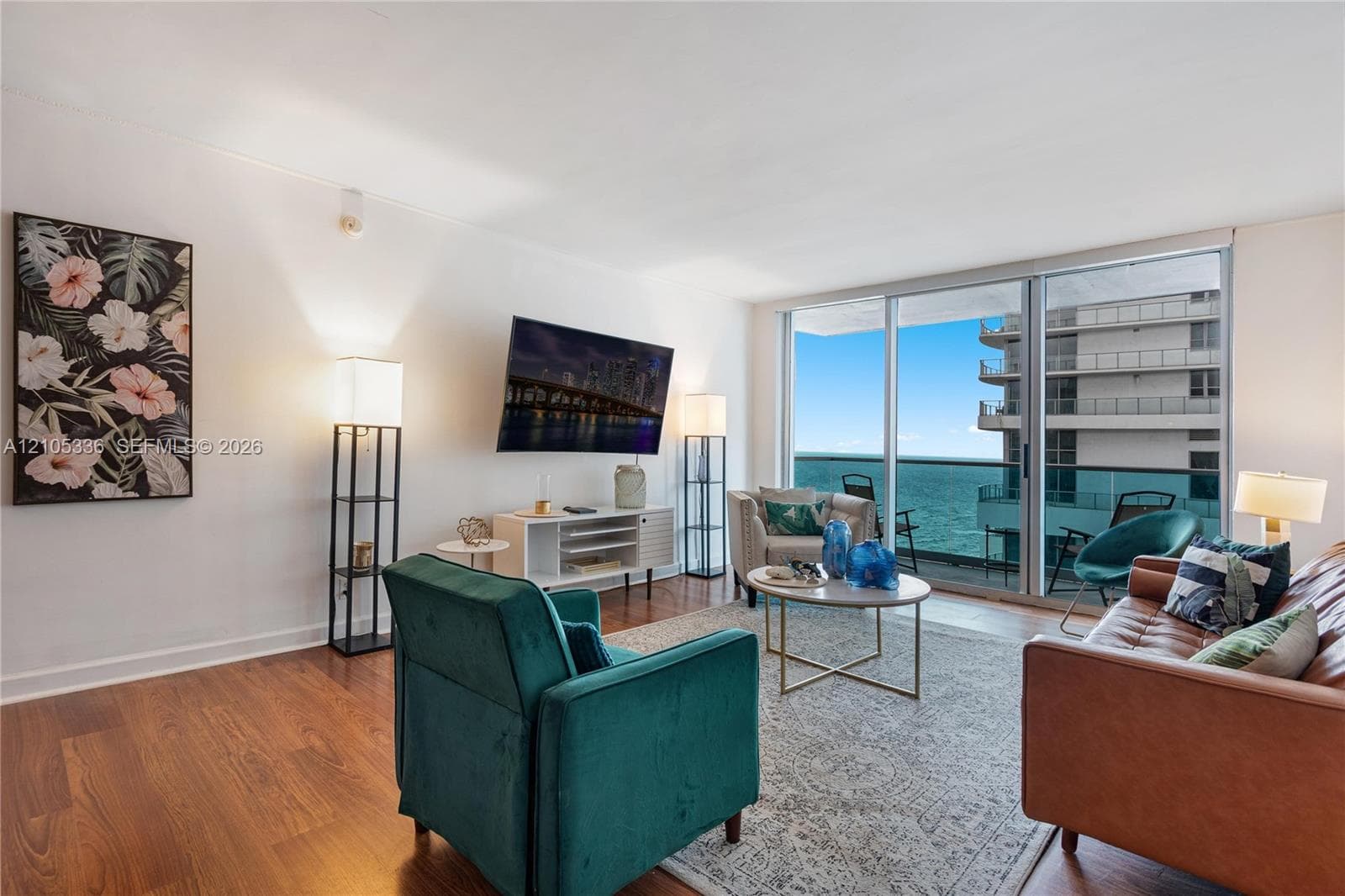 Living area featuring wood-finish flooring and expansive glass sliding doors providing external access to a balcony with water scenery