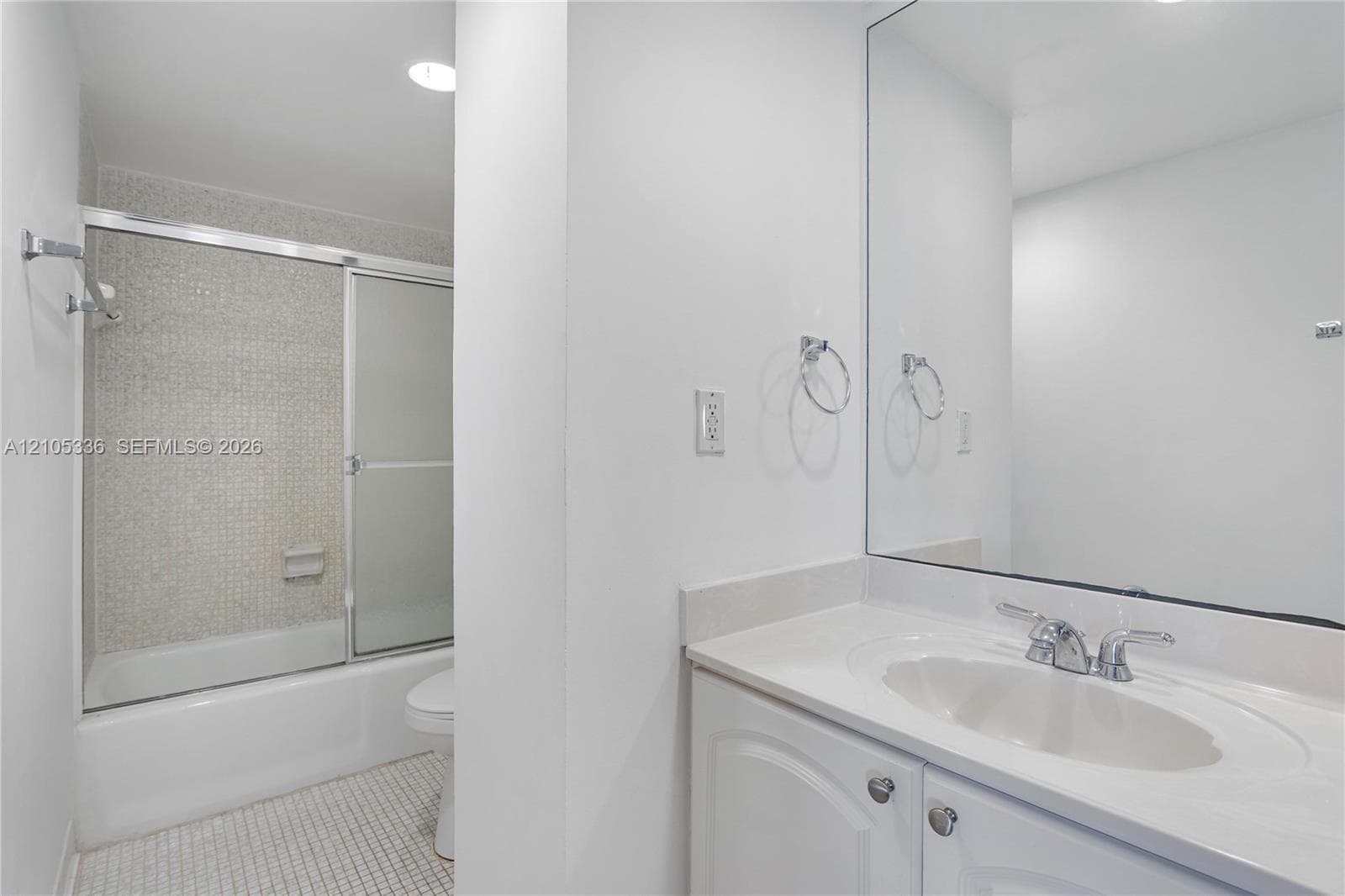 Bathroom featuring a vanity with integrated sink, expansive wall-mounted mirror, soaking tub with sliding glass enclosure, and mosaic floor tiling