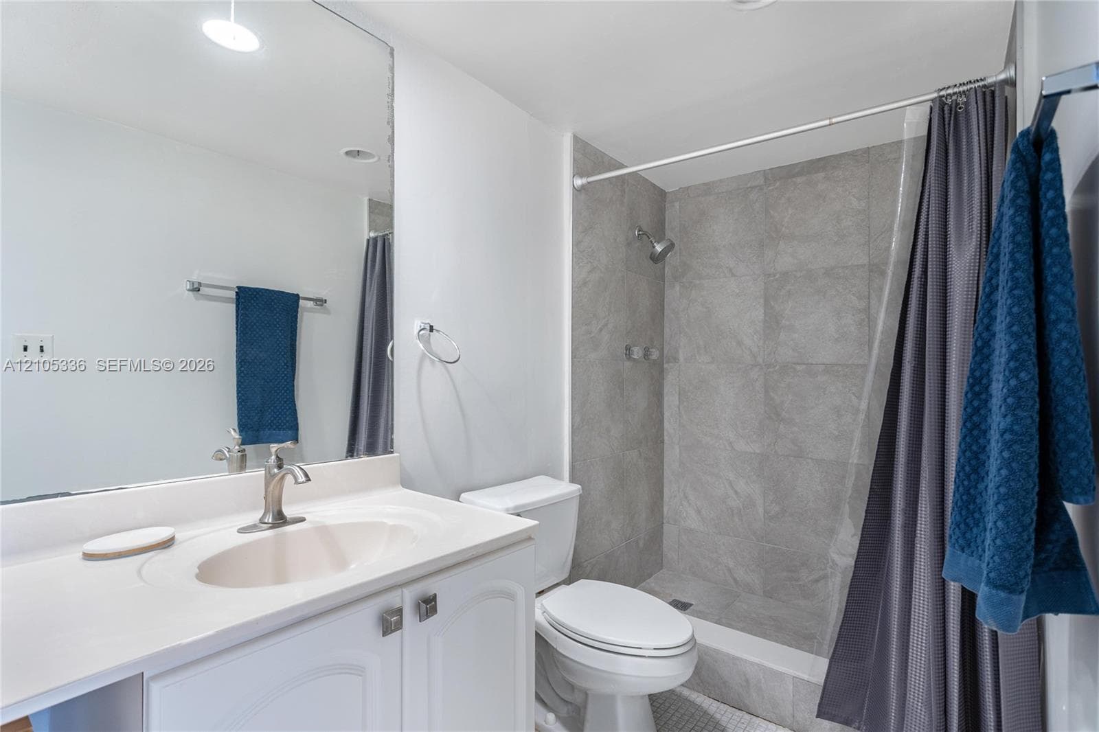 Bathroom featuring a vanity with an integrated sink and solid-surface countertop, full-width mirror, and a tub-shower combination with large-format grey tile surround