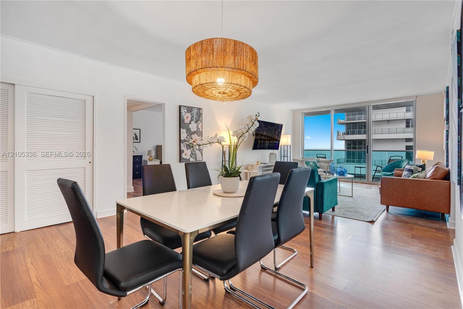 Open-concept interior featuring wood-finish flooring, floor-to-ceiling glass sliding doors, textured tiered drum pendant lighting, and louvered double-door closets