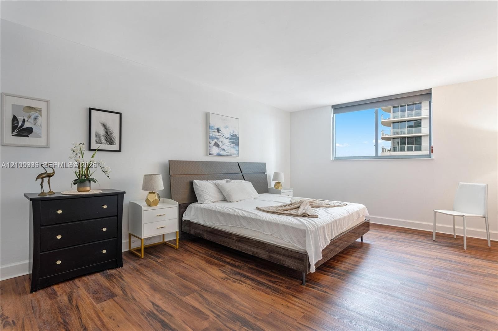Room featuring wood-finish flooring, a large window with roller shade, and neutral wall tones