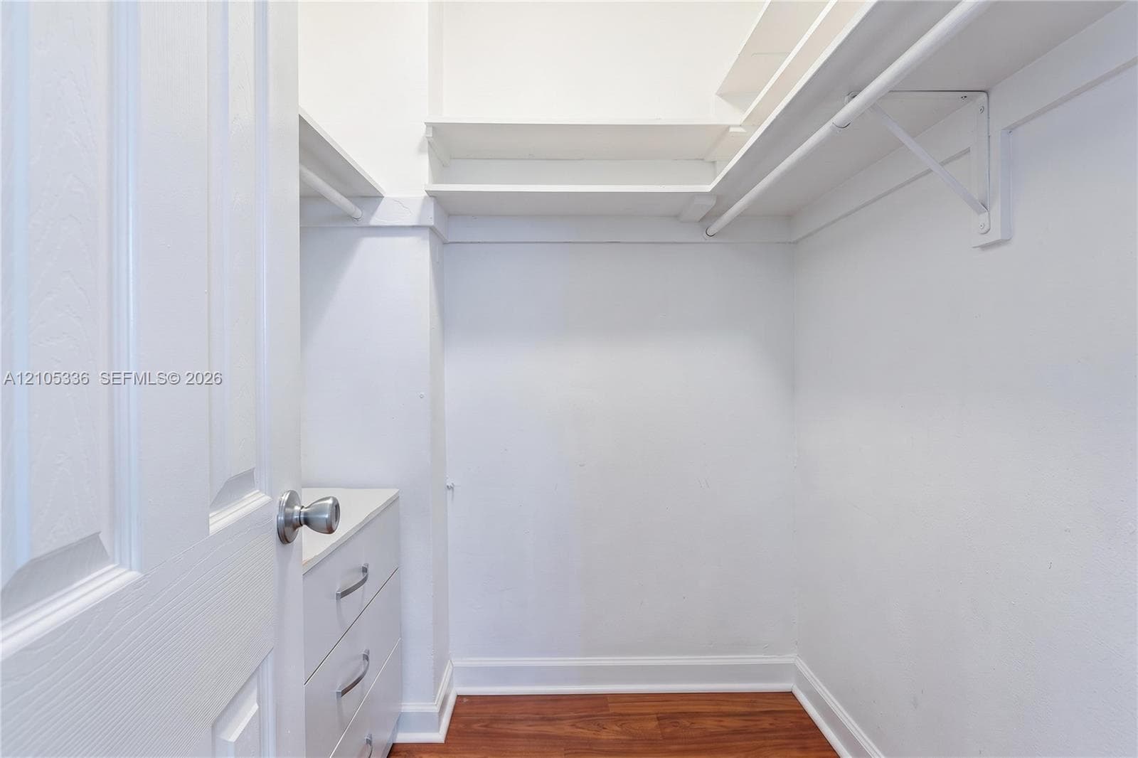 Walk-in closet featuring wood-finish flooring, built-in shelving, hanging rods, and integrated drawer cabinetry