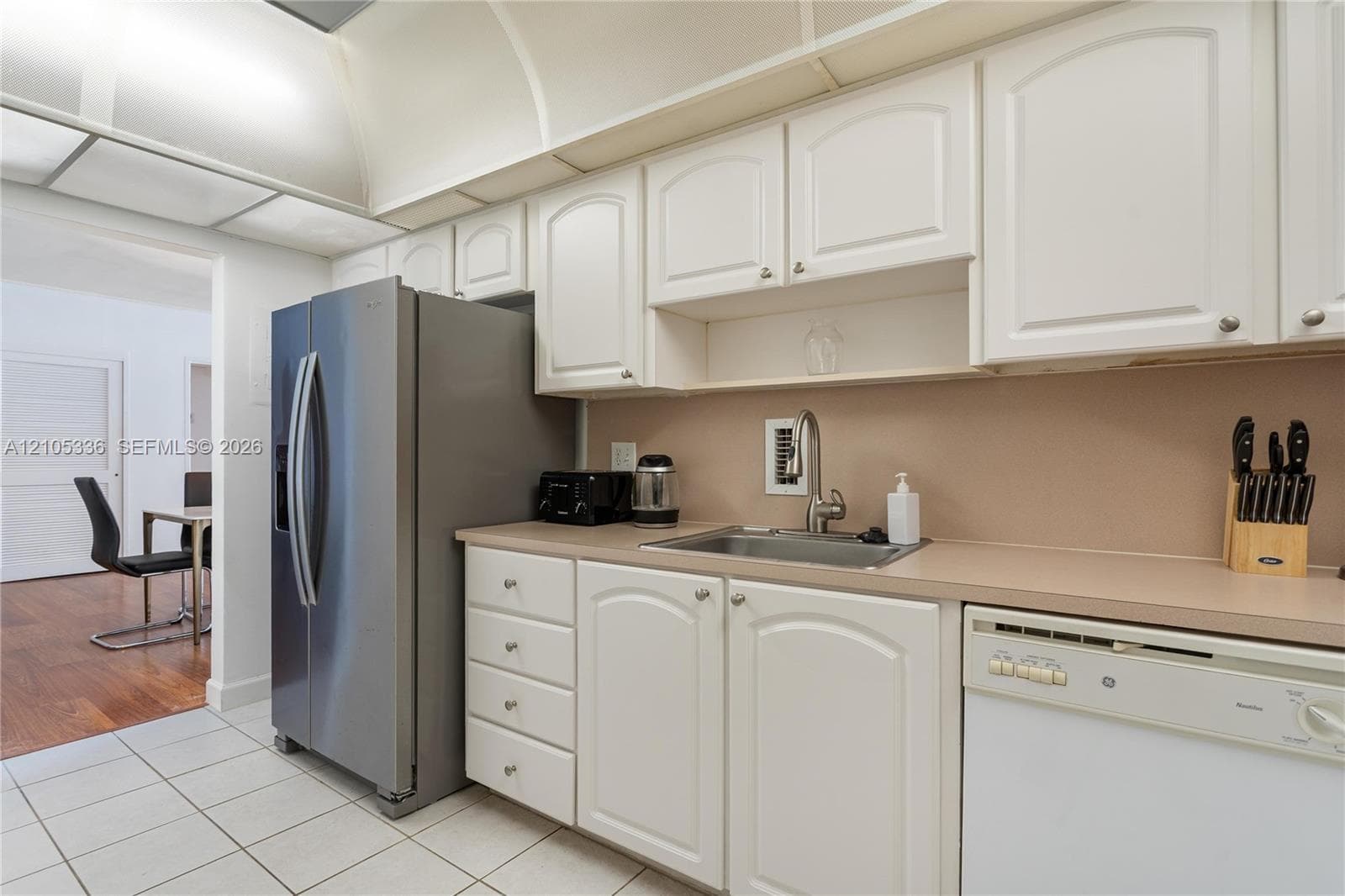Kitchen featuring white shaker-style cabinetry, solid-surface countertops, stainless steel side-by-side refrigerator, under-mount sink with pull-down faucet, and tiled flooring