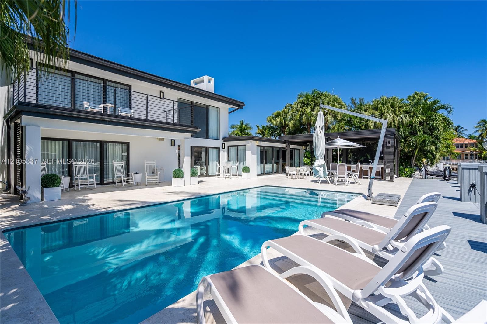 Contemporary exterior featuring a multi-level balcony with metal railings, an inground pool with stone decking, and a covered outdoor kitchen area