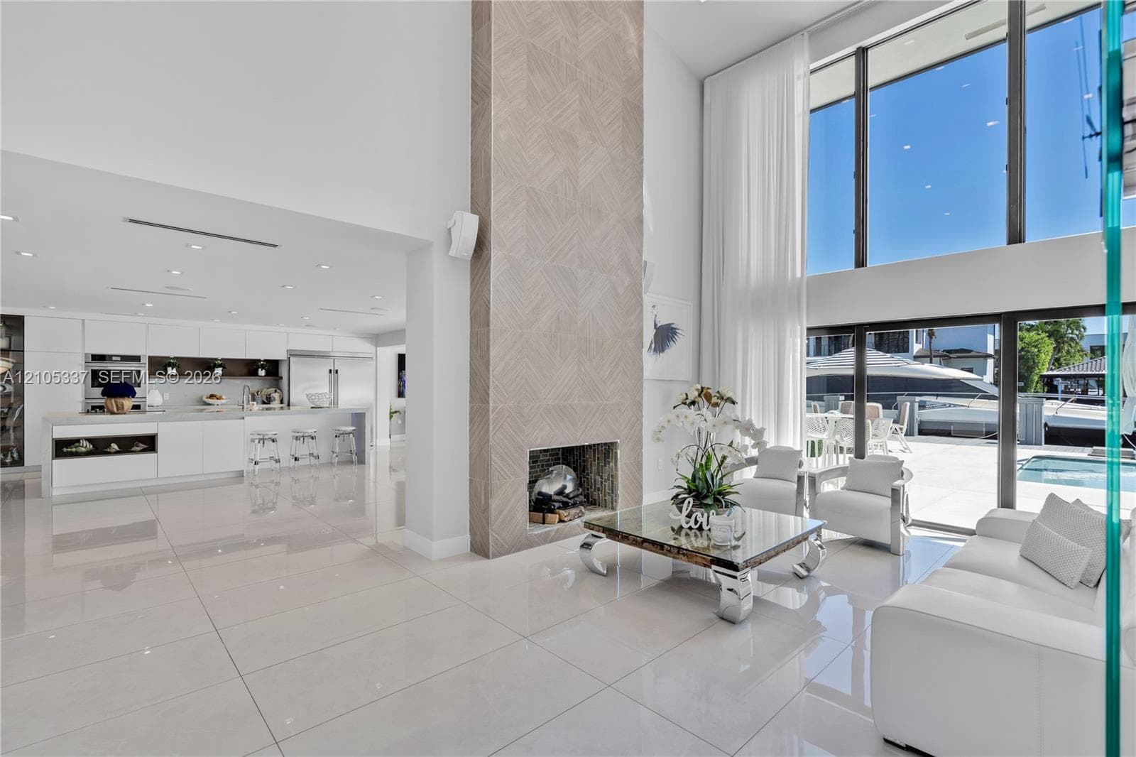 Double-height living area featuring floor-to-ceiling windows, porcelain tile flooring, recessed lighting, and a floor-to-ceiling fireplace with geometric stone surround