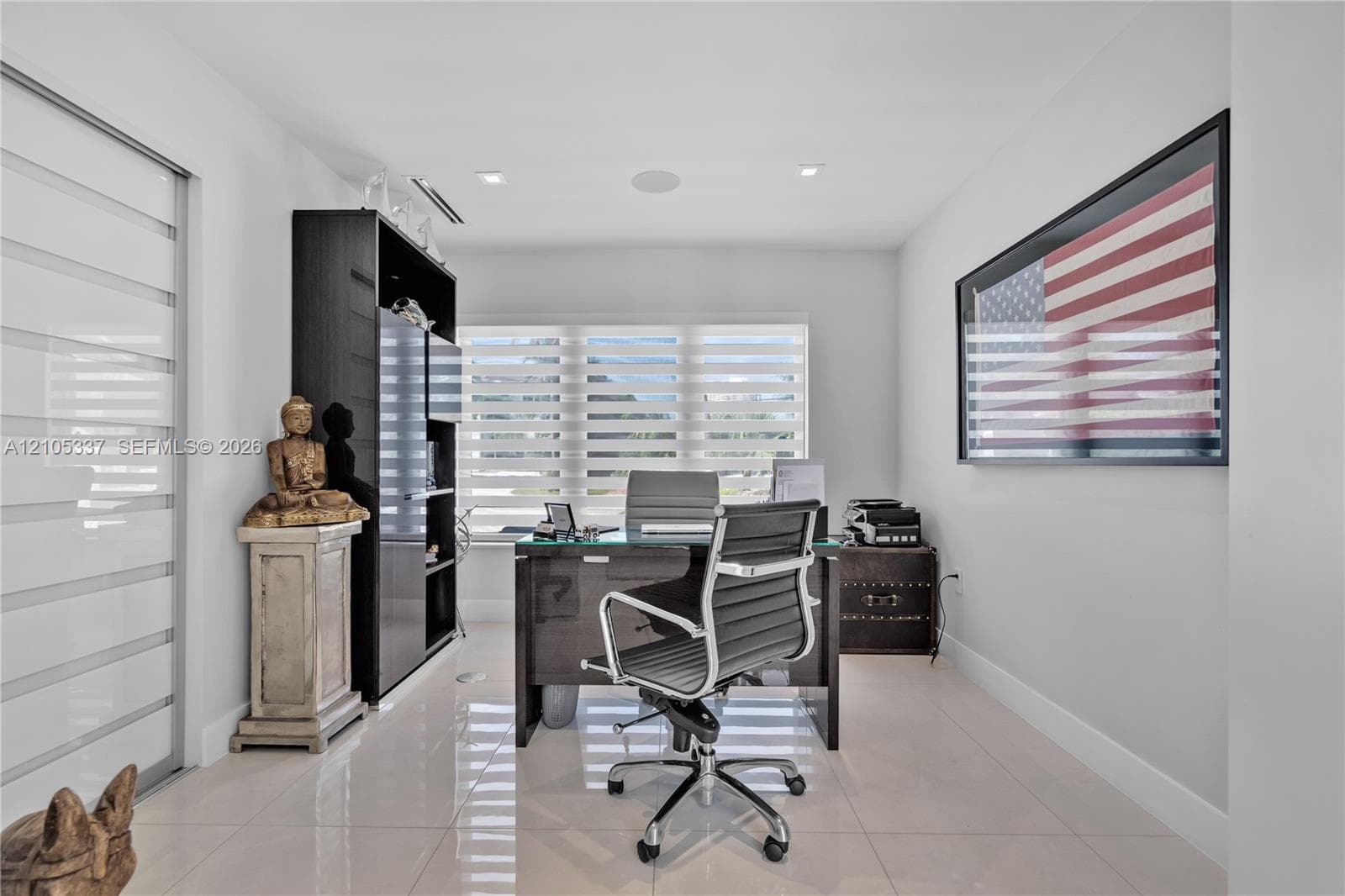Neutral-toned interior featuring large-format tile flooring, recessed ceiling lighting, horizontal blinds, and a built-in dark cabinetry unit