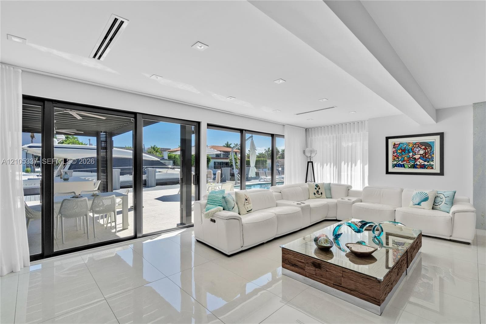 Large-format porcelain tile flooring, recessed ceiling lighting, and expansive floor-to-ceiling sliding glass doors opening to a covered outdoor patio