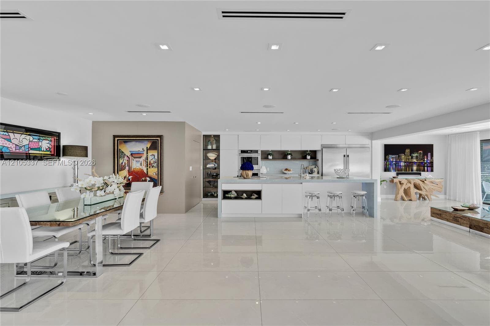 Open-concept kitchen featuring minimalist white cabinetry, a large central island with seating, polished stone-finish flooring, and recessed ceiling lighting