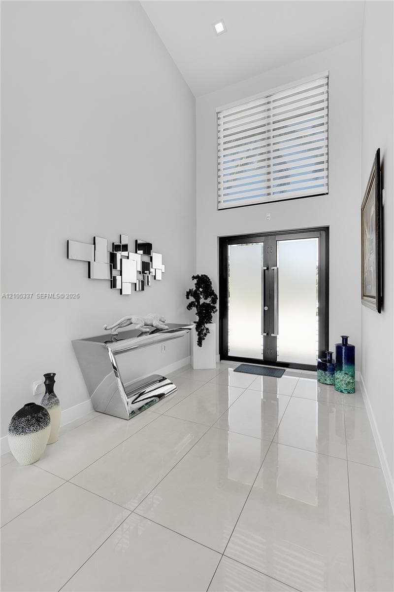 Foyer featuring double entry doors with frosted glass, high ceilings, large-format polished tile flooring, and a transom window
