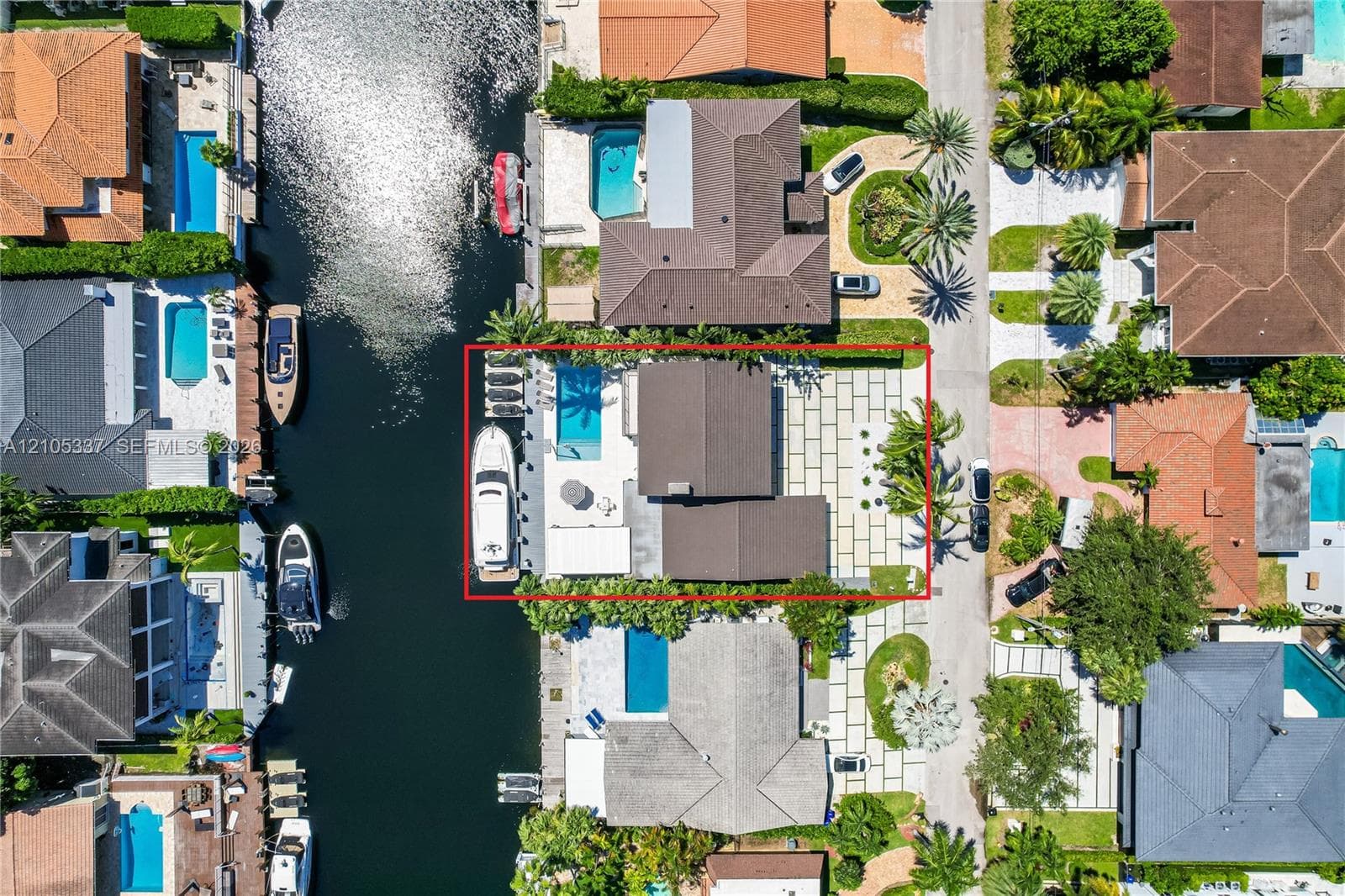 Waterfront property featuring a private boat dock, in-ground swimming pool, expansive stone paver patio, and mature palm trees